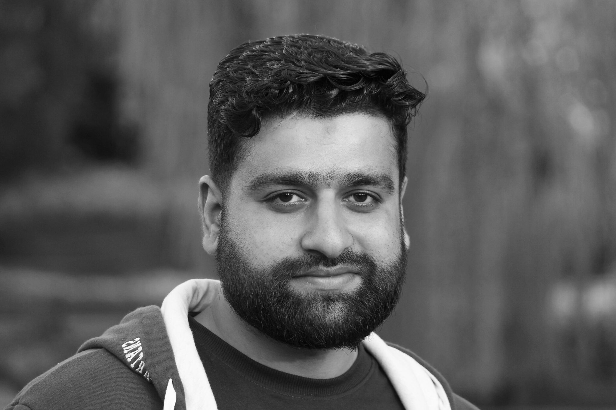 Black and white close-up portrait of a bearded man with a neutral expression.